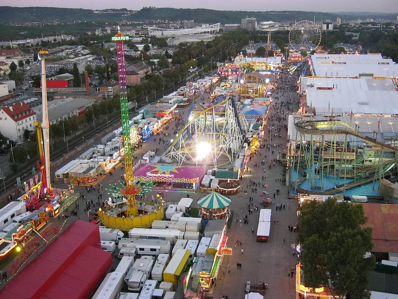 Manèges, tentes et allées du Cannstatter Volksfest vus d’en haut au crépuscule.