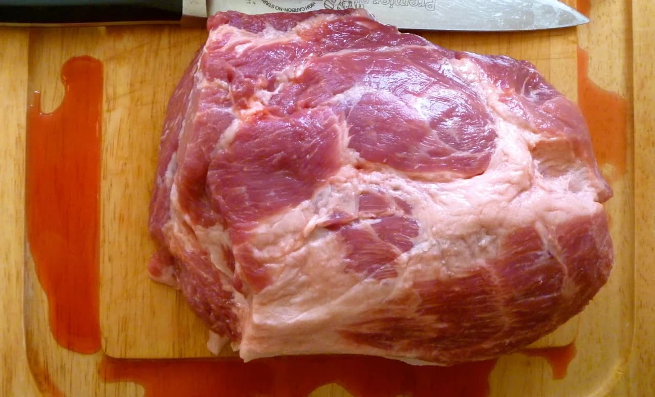 Pièce de porc crue avec gras et tissu conjonctif visibles sur une planche.