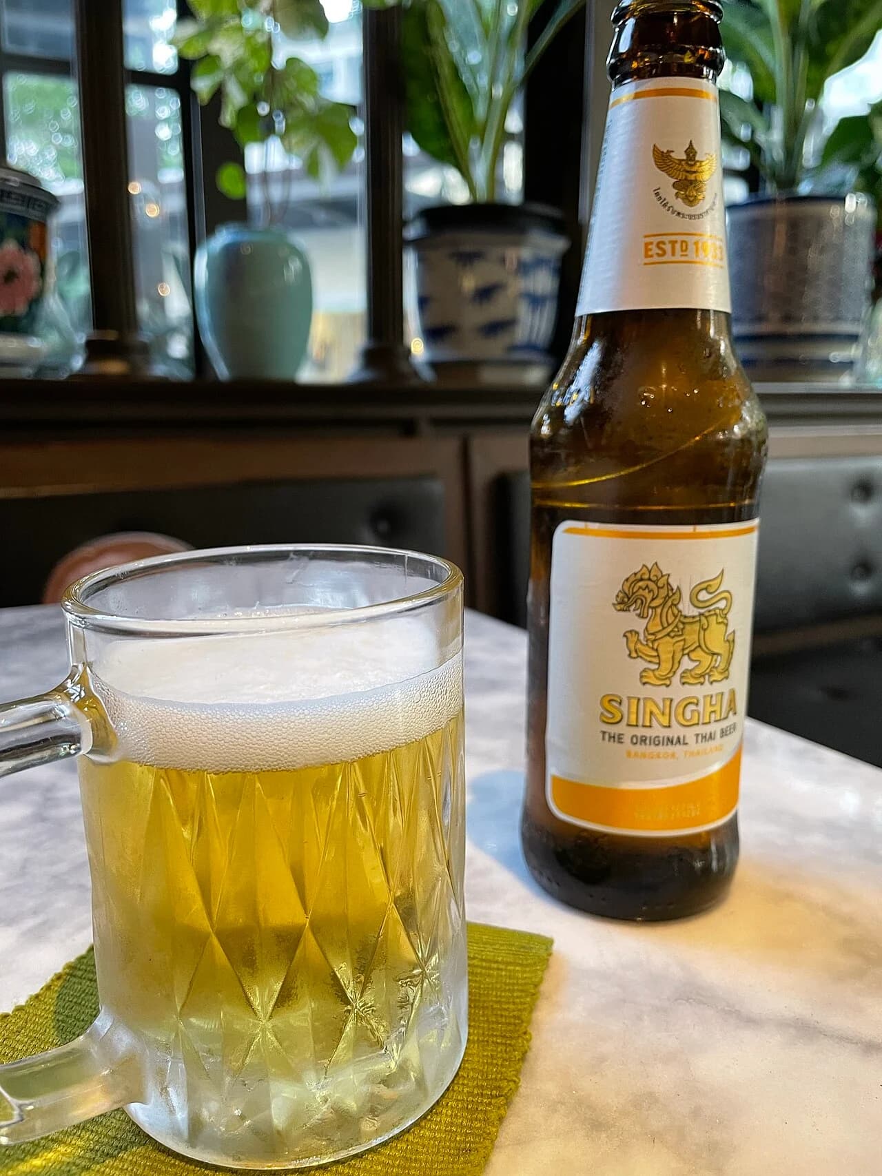 Bouteille étiquetée Singha et verre de bière claire.