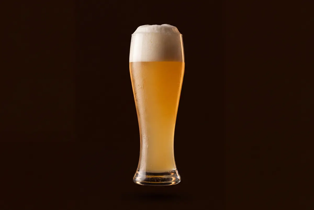 Verre de bière blanche trouble sous un col de mousse dense.