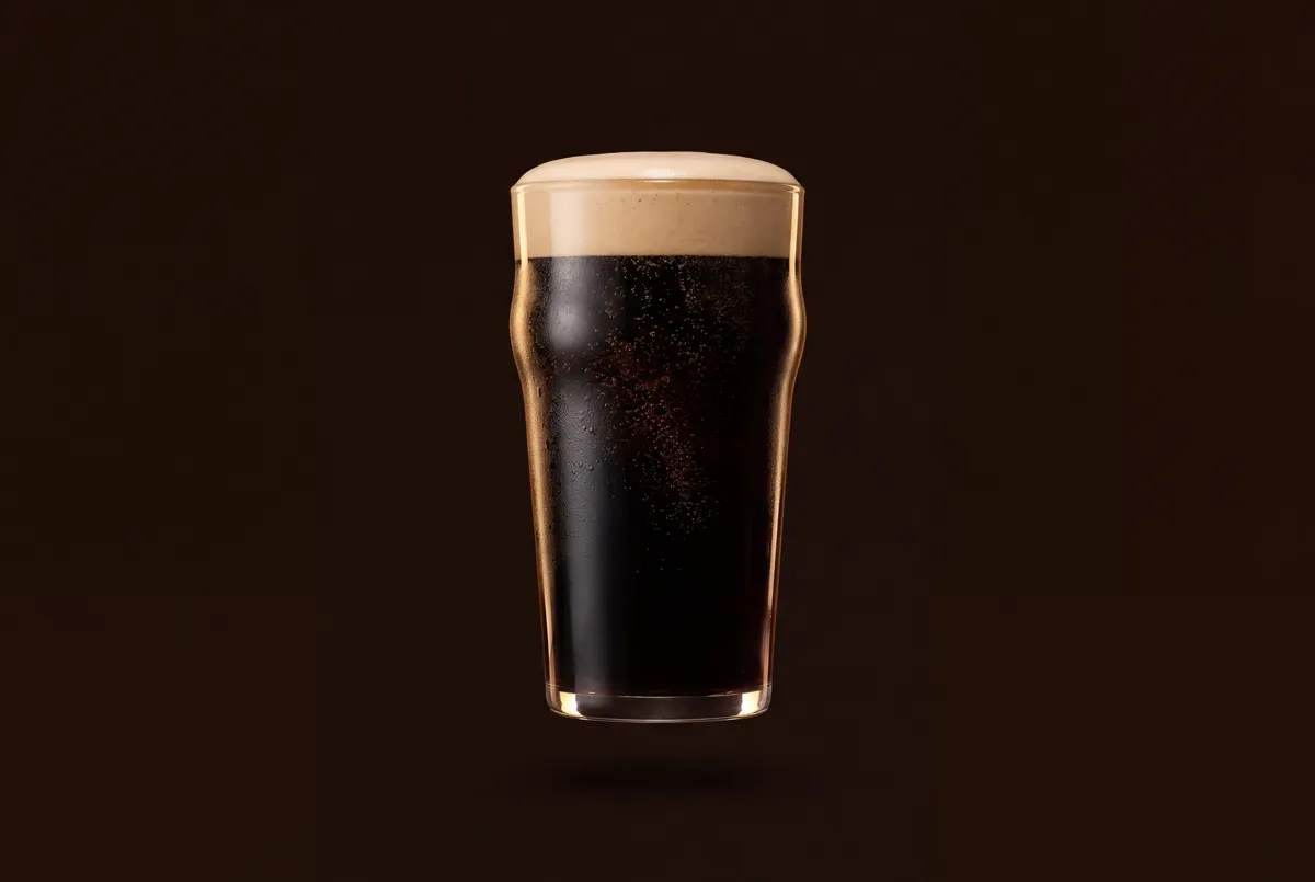 Verre de stout noire opaque surmonté d’une mousse crémeuse beige au dôme lisse.